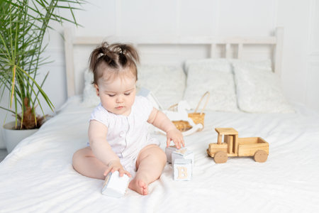 baby girl playing with wooden toy cubes on the bed at home in a bright room, the concept of early...