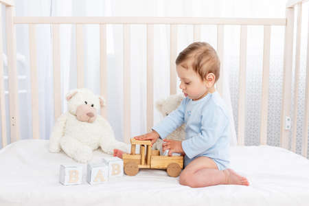 baby boy in the crib in the children's room with wooden toys on a cotton white bed playingの写真素材