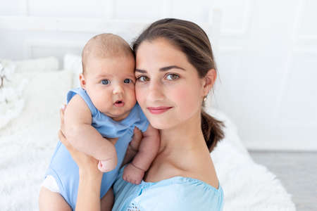 a young mother with a newborn baby gently embraces him at home on the bed, the concept of a happy family and birthの写真素材