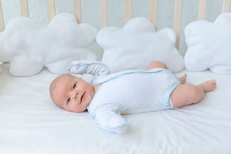 newborn baby boy smiles lying on the back of the crib on the cotton bed at home before going to bed, baby week, the concept of birth and infancy.の写真素材