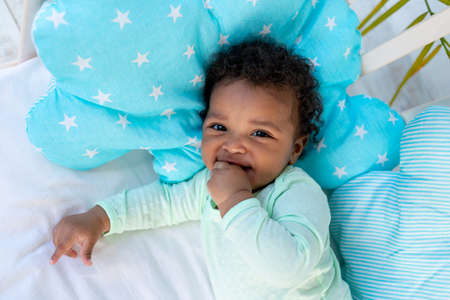 a laughing African baby lies on its back on a bed at home on a blue cotton bed and smilesの写真素材