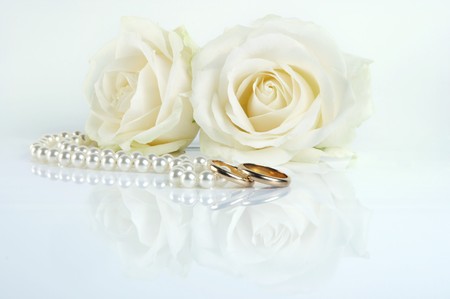 Two golden wedding rings and two white roses on a reflecting white surfaceの写真素材