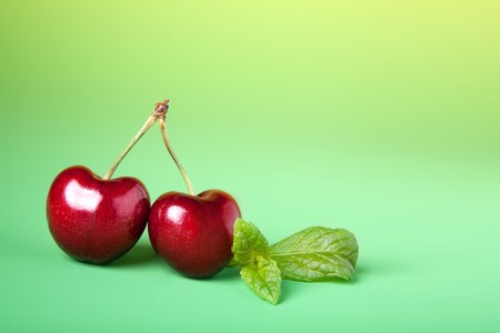 Two perfect specimen of red cherries on a green backgroundの写真素材