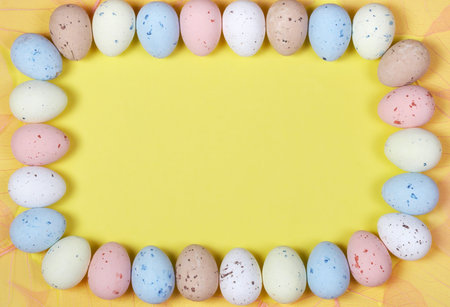 Frame with text space, made of pastel colored easter eggs and pink feathers