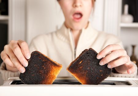 Hands of a woman taking burnt toast out of a toasterの写真素材