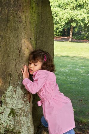 Little girl putting her ear against a large tree, listening to the gnomesの写真素材