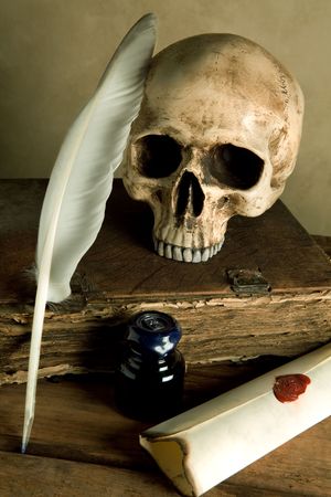 Skull and antique book on a table with old parchment and quillの写真素材