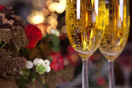 Flower arrangement and champagne glasses in front of a blurred christmas treeの写真素材