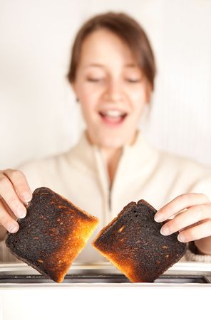 Surprised woman taking burnt toast out of a toasterの写真素材