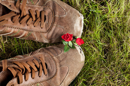 Two old boots in grass sharing love and two little red rosesの写真素材