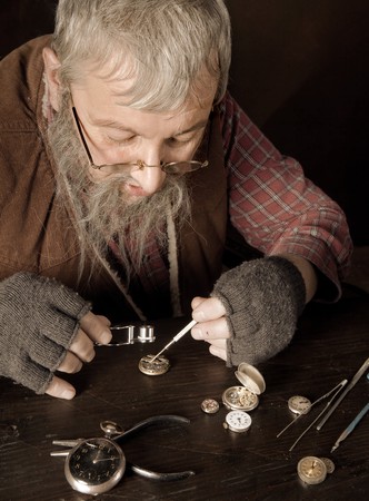 Old bearded man reparing antique watches using a magnifying glassの写真素材