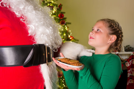 Adorable girl presenting cookies to santa claus