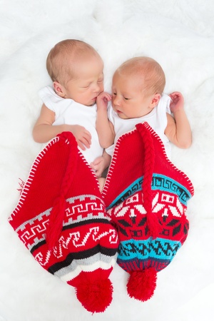 Tiny newborn twins sleeping inside knitted red hatsの写真素材