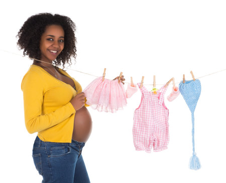 Happy pregnant african woman hanging baby laundry on a line