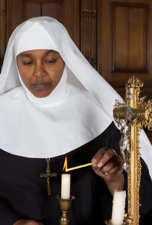 Mature nun lighting a candle on the altar of a medieval churchの写真素材