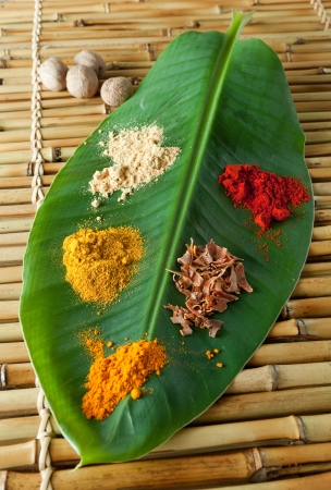 Exotic display of spices on a green banana leaf like curcuma, pepper, nutmeg, paprika and curryの写真素材