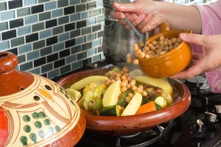 Moroccan woman adding chickpeas to her tajine pot while preparing dinner during ramadanの写真素材
