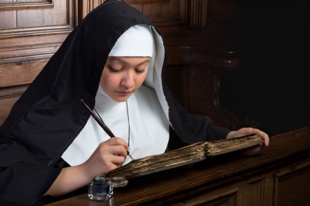 Vintage scene of a young nun writing in an ancient bookの写真素材