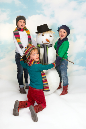 Three happy girls dancing round the snowmanの写真素材