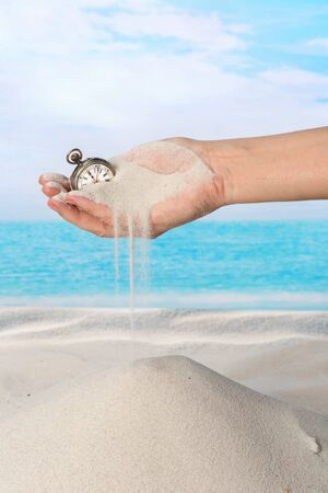 Hand with pocket watch and sand flowing on the beachの写真素材