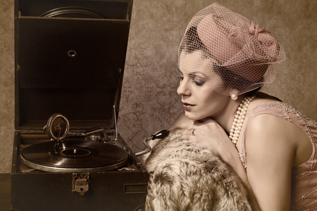 Vintage 1920s style lady in pink listening to an antique record playerの写真素材