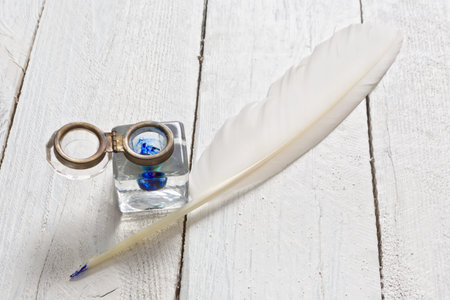 Feather quill and blue ink pot on a rustic white painted tableの写真素材
