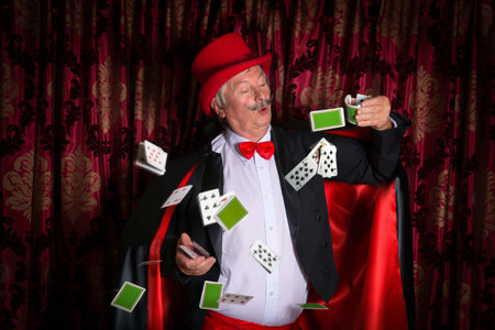 Mature magician on stage performing a magic trick with cards