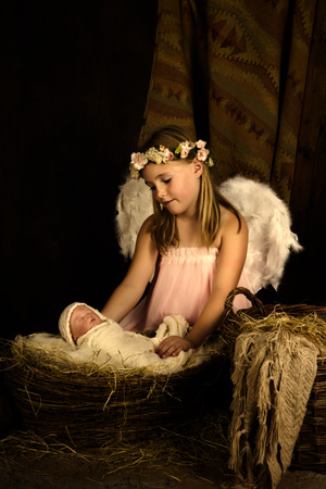 Pink little girl playing an angel in a Christmas nativity scene with a dollの写真素材
