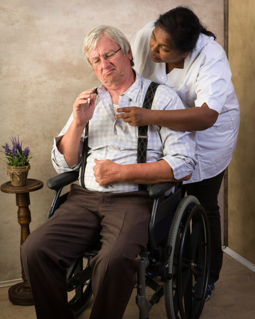 Grumpy old grandpa in nursing home receiving medication by a nurseの写真素材