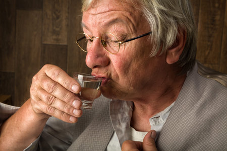 Gray elderly man enjoying a jenever drink in a shot glassの写真素材