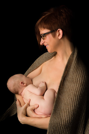 Young mother breastfeeding her 7 week old baby against black background