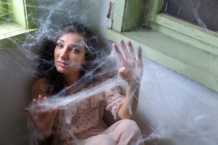 Young scared woman trapped in a corner with cobwebs or spiderwebsの写真素材