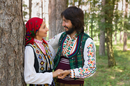Romantic couple posing in a forest wearing traditional Bulgarian clothing