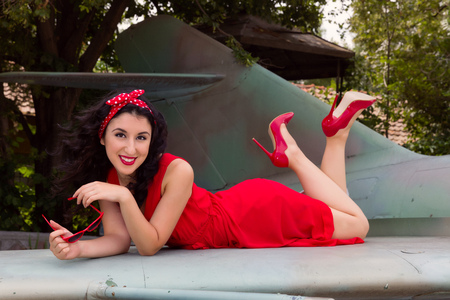 Sexy pin-up model in flashy red dress posing on a wing of a WW2 airplaneの写真素材