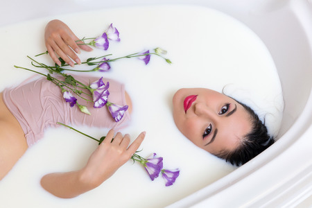 Relaxed young woman in skintone top enjoying a milk bath with flowersの写真素材