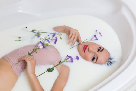 Relaxed young woman in skintone top enjoying a milk bath with flowersの写真素材