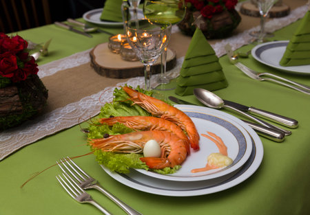 Festive dinner table with flower arrangements and decor napkins and christmas tree in the backgroundの写真素材