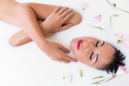 Elegant young woman relaxing in a milk bath with flowers