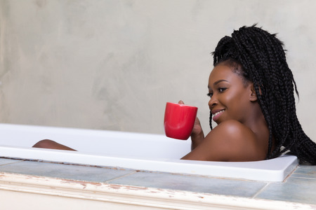 Beautiful woman with afro hair dreaming in bath tubの写真素材