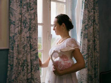 Young woman in authentic regency dress near a window of a classical interiorの写真素材