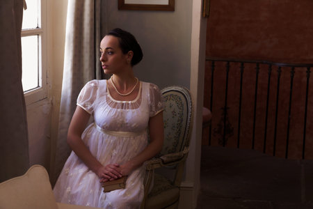 Young woman in authentic regency dress near a window of a classical interior