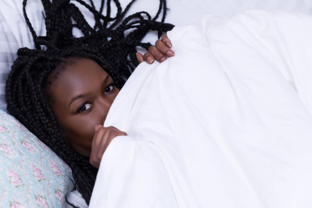 Beautiful African woman with long braids relaxing on her bed in the morning