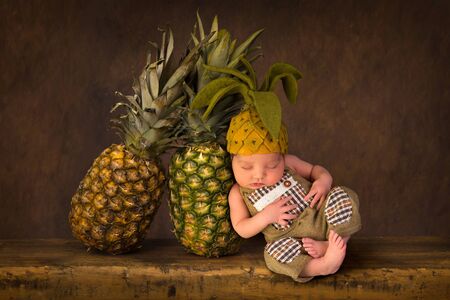 Cute composite image with fresh pineapples and a newborn baby in felted pineapple hatの写真素材