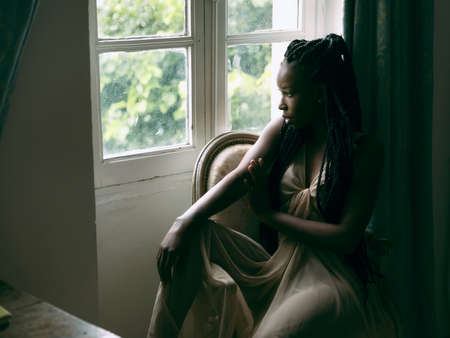 Beautiful woman in sheer nightgown looking out of a window with backlightingの写真素材