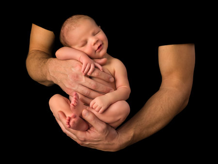 Hands of a young father holding his 7 days old newborn baby boy against a black background