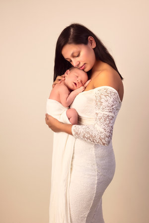 Beautiful young mother in a white lace gown posing with her 7 days old newborn sonの写真素材