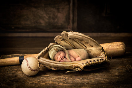Newborn baby sleeping in an old leather baseball gloveの写真素材