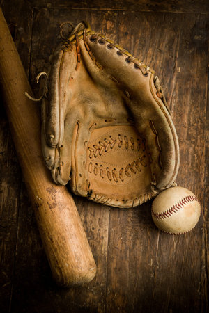 Old leather baseball glove lying on an antique table with ball and bat
