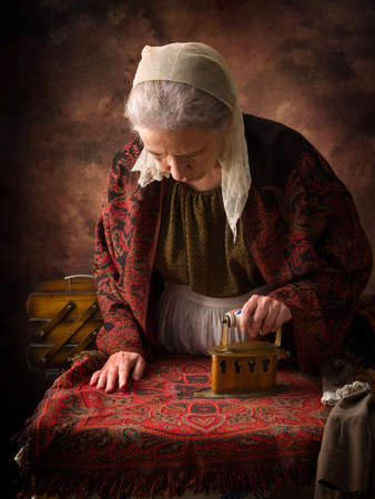 Old woman in victorian dress working with an antique charcoal iron on a boardの写真素材