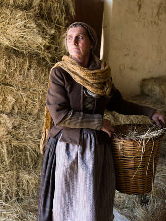 Woman in historical medieval costume posing with a wicker basket in a hay barnの写真素材